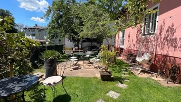 Sonnige Gartenterrasse mit Sitzgelegenheiten und üppiger Bepflanzung neben dem Haus.