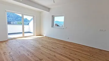 Helles Wohnzimmer mit Holzboden, Zugang zum Balkon und Bergblick.