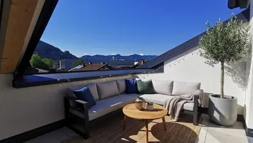 Sonnige Dachterrasse mit bequemen Outdoor-Möbeln und weitem Bergblick.