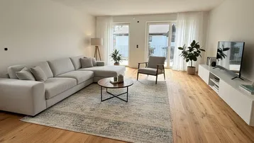 Helles Wohnzimmer mit modernem Sofa, Holzboden und Zugang zu einem Außenbereich.