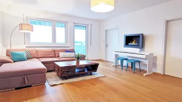 Helles Wohnzimmer mit beigem Ecksofa, Holzboden und einem modernen Wandkamin.
