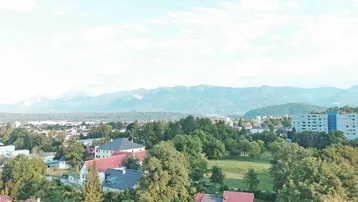 Weitläufiger Blick über eine grüne Landschaft mit Bergen im Hintergrund und städtischer Bebauung.