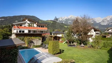 Großer Garten mit Pool, Spielplatz und beeindruckendem Bergblick unter blauem Himmel.