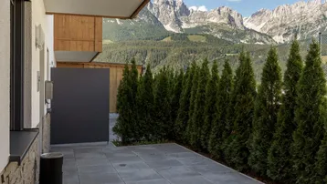 Gepflasterte Terrasse mit Heckenbegrenzung und beeindruckendem Blick auf die umliegende Berglandschaft.