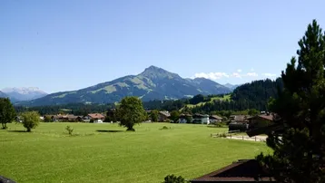 Weitläufiger Blick über grüne Wiesen und ein Dorf auf die majestätischen Berge im Hintergrund.