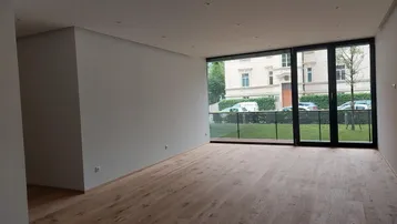Helles, leeres Zimmer mit Holzboden und großen Fenstern, die auf die Straße blicken.