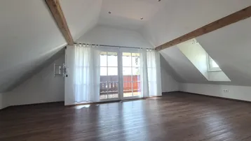 Helles Dachgeschosszimmer mit Holzbalken, dunklem Holzboden und Zugang zu einem Balkon.