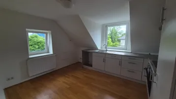 Küche mit Einbauschränken, Spüle und Herd, unter Dachschrägen mit Fenstern.