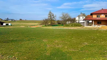 Weitläufige Grünfläche mit Blick auf die umliegende Landschaft und einige Wohnhäuser in der Ferne.