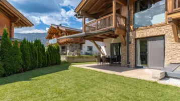 Geräumiger Gartenbereich mit Rasenfläche und einer möblierten Terrasse vor dem Holzchalet.