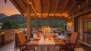 Gemütliche Holzterrasse mit Esstisch, Lichterketten und Bergblick bei Sonnenuntergang.