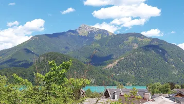 Panoramablick auf Berge und See mit Häuserdächern im Vordergrund unter blauem Himmel.