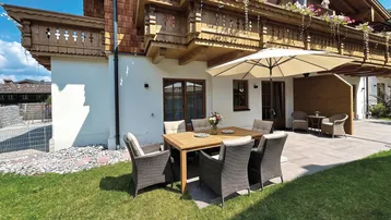 Gemütliche Terrasse mit Gartenmöbeln und Sonnenschirm vor einem traditionellen Holzhaus.
