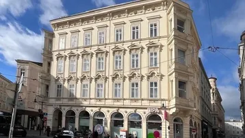 Historisches Eckgebäude mit klassischer Architektur und Geschäften im Erdgeschoss an einer belebten Straße.