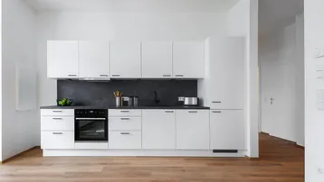 Moderne, offene Küche mit weißen Schränken, dunkler Arbeitsplatte und hellem Holzfußboden.