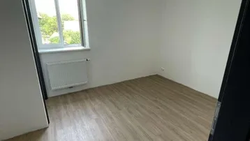 Leerer Raum mit Laminatboden und einem Fenster, das eine grüne Aussicht bietet.