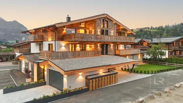 Majestätisches Chalet mit traditioneller Holz- und Steinfassade, umgeben von alpiner Landschaft bei Sonnenuntergang.