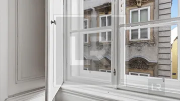 Fenster mit Blick auf eine historische Gebäudefassade mit Stuckverzierungen und klassischen Details.