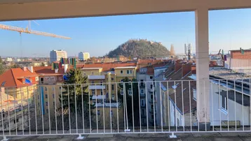 Weitblick von der Terrasse über die Stadt mit Gebäuden und einem Hügel im Hintergrund.