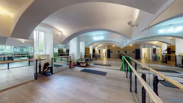 Geräumiger Fitnessraum mit hohen Gewölbedecken, Spiegelfronten und Holzboden, ideal für Sportaktivitäten.