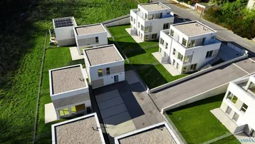 Luftaufnahme einer modernen Wohnsiedlung mit weißen Gebäuden, grünen Rasenflächen und Flachdächern.