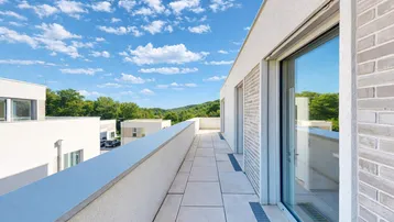Langer Balkon mit Fliesenboden und weitem Blick über die umliegende Landschaft und Bäume.