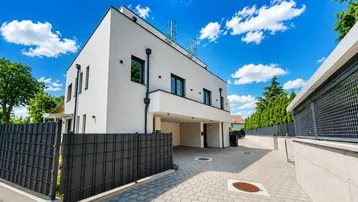 Modernes Mehrfamilienhaus mit weißer Fassade, Carport und gepflasterter Zufahrt unter blauem Himmel.