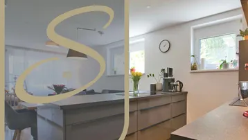 Moderne Küche mit Kücheninsel, großen Fenstern und Holzboden, offen zum Essbereich hin.