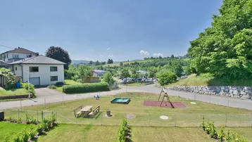 Weitläufiger Blick auf den Spielplatz und die umliegende grüne Landschaft mit Wohnbebauung.