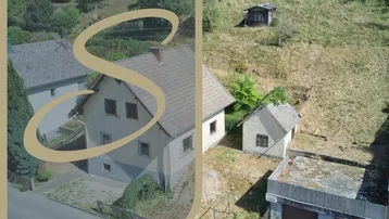 Luftaufnahme eines Hauses mit Satteldach und einem Nebengebäude auf einem Hanggrundstück.