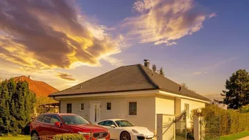 Einfamilienhaus mit gepflegter Auffahrt und zwei Fahrzeugen unter einem dramatischen Abendhimmel.