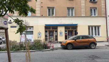 Ansicht der Gebäudefassade mit mehreren Fenstern und einem geparkten orangefarbenen Auto davor.