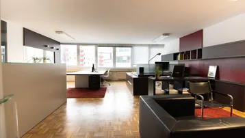 Geräumiges und helles Büro mit mehreren Arbeitsplätzen, Holzparkettboden und großen Fenstern.