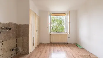 Leerer Raum mit Laminatboden und Fenster, vorbereitet für eine neue Küche.