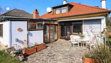 Gepflasterte Terrasse mit Gartenmöbeln und Zugang zum Wintergarten, umgeben von Grünflächen.