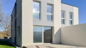 Moderne Neubaufassade mit großen Fenstern und einer kleinen Terrasse im Erdgeschoss.