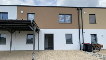 Mehrere Reihenhäuser mit Carport und gepflasterter Terrasse im Außenbereich.