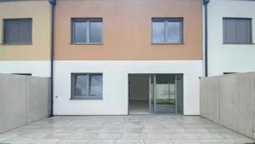 Rückseite eines Reihenhauses mit gepflasterter Terrasse und kleinem Rasenbereich.