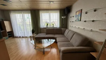 Gemütliches Wohnzimmer mit großem Ecksofa, Holzbalkendecke und Zugang zu einem Balkon.