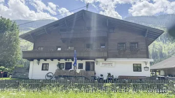 Traditionelles Holzhaus in den Bergen mit Balkonen und weiß getünchter Fassade, umgeben von grüner Natur.