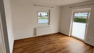 Helles Zimmer mit Laminatboden, weißen Wänden und Zugang zu einem Außenbereich, ausgestattet mit Heizkörper.