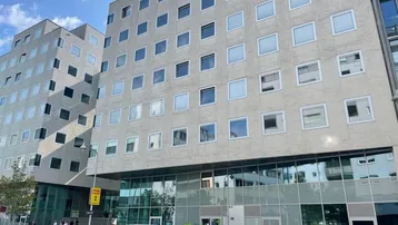 Moderne Bürogebäude-Fassade mit vielen Fenstern und einem verglasten Erdgeschossbereich, davor parken Autos.