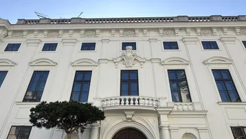 Klassische weiße Fassade eines historischen Gebäudes mit symmetrischen Fenstern und einem kleinen dekorativen Balkon.