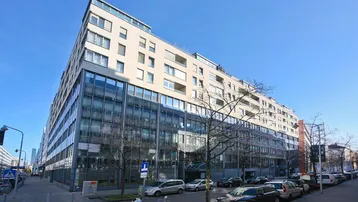 Modernes Büro- und Wohngebäude mit Glasfassade und mehreren Etagen an einer städtischen Straße.