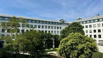 Blick auf die moderne Gebäudefassade mit einem begrünten Innenhof und klarem blauen Himmel.
