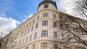 Historisches Gebäude mit eleganter Fassade, vielen Fenstern und einem markanten Kuppeldach unter blauem Himmel.