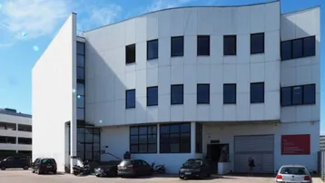Modernes Geschäftsgebäude mit geschwungener Fassade und Parkplätzen davor unter blauem Himmel.