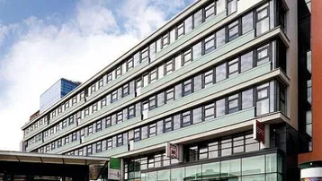 Modernes Geschäftsgebäude mit vielen Fenstern und Glasfassade im Erdgeschoss, belebtem Gehweg davor.