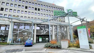 Modernes Bürogebäude mit Betonfassade, großen Fenstern und einem Eingangsbereich mit Beschilderung.