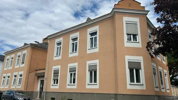 Historisches Gebäude mit helloranger Fassade und weißen Fensterrahmen an einer Straße gelegen.